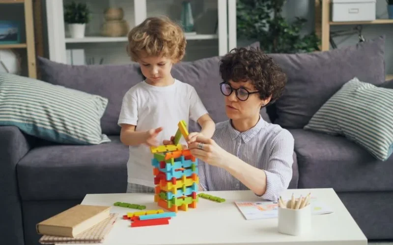 A mother and son playing with colorful building blocks on a table in a cozy living room.