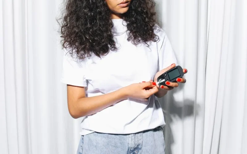 A woman using a glucometer to check blood sugar levels indoors, highlighting diabetes care.