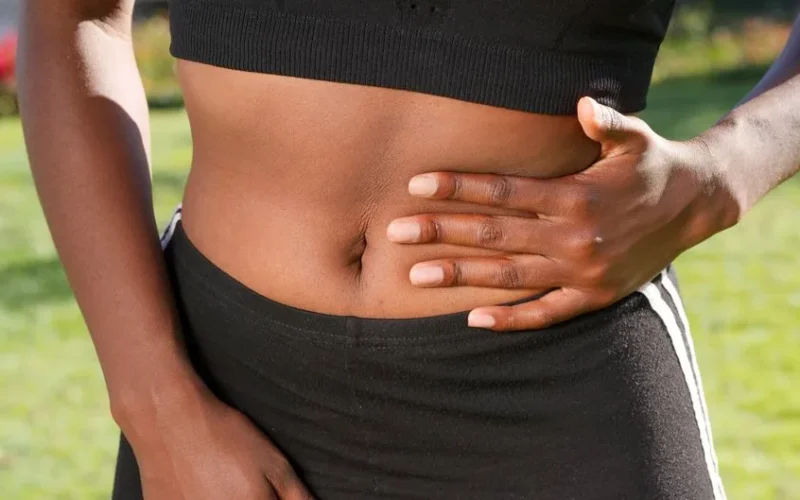 Close-up of a person holding their abdomen, indicating stomach discomfort, outdoors.