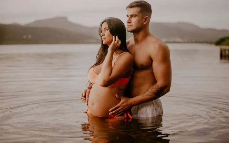 Pregnant woman and partner enjoying a peaceful moment in a lake, radiating love and serenity.