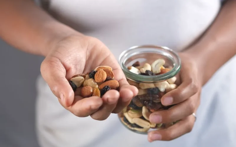 A person's hands holding a glass jar and a handful of assorted nuts, perfect for healthy snacking.