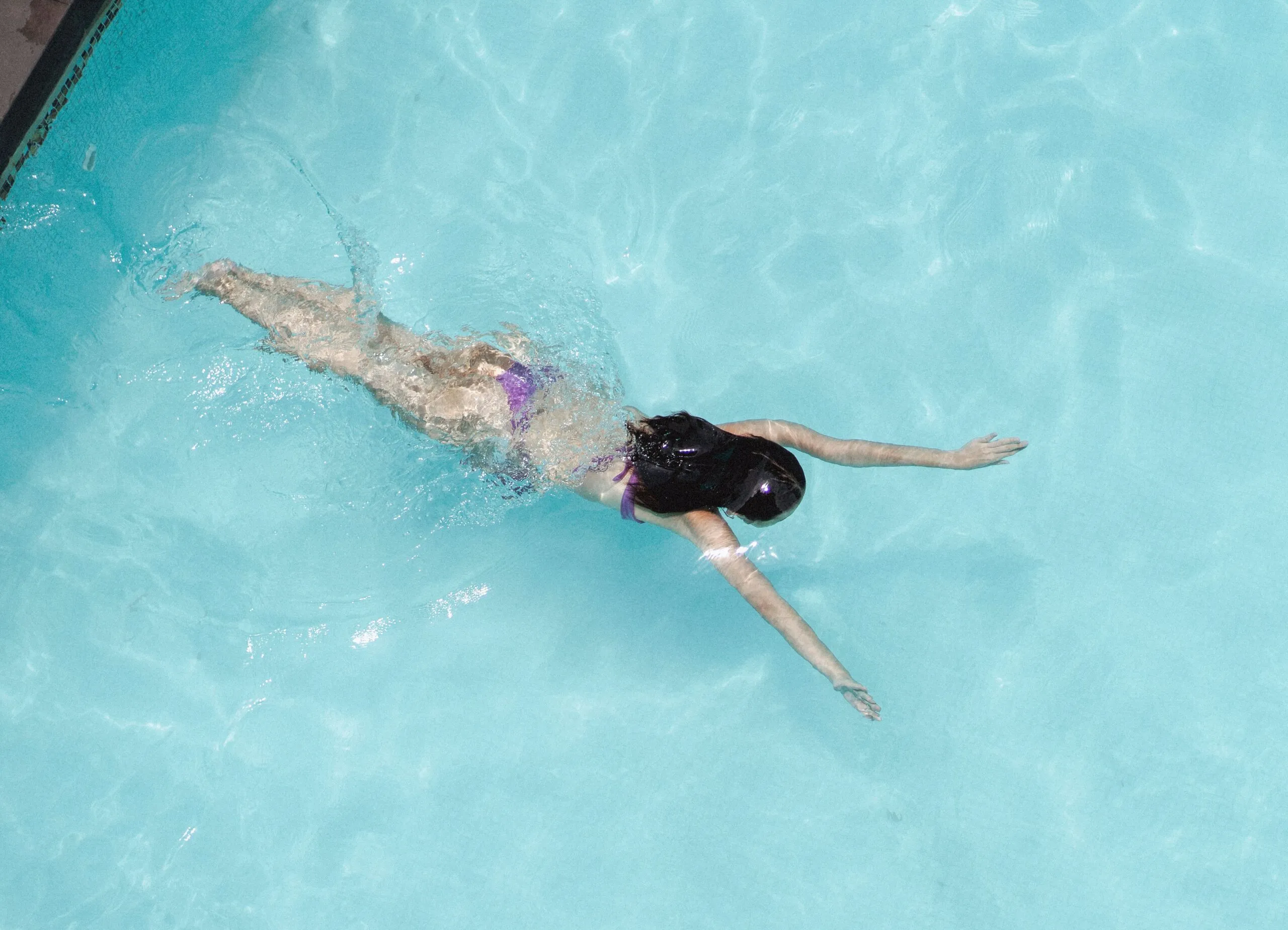 Top view of anonymous slim lady floating underwater in crystal clear blue water in swimming pool on resort