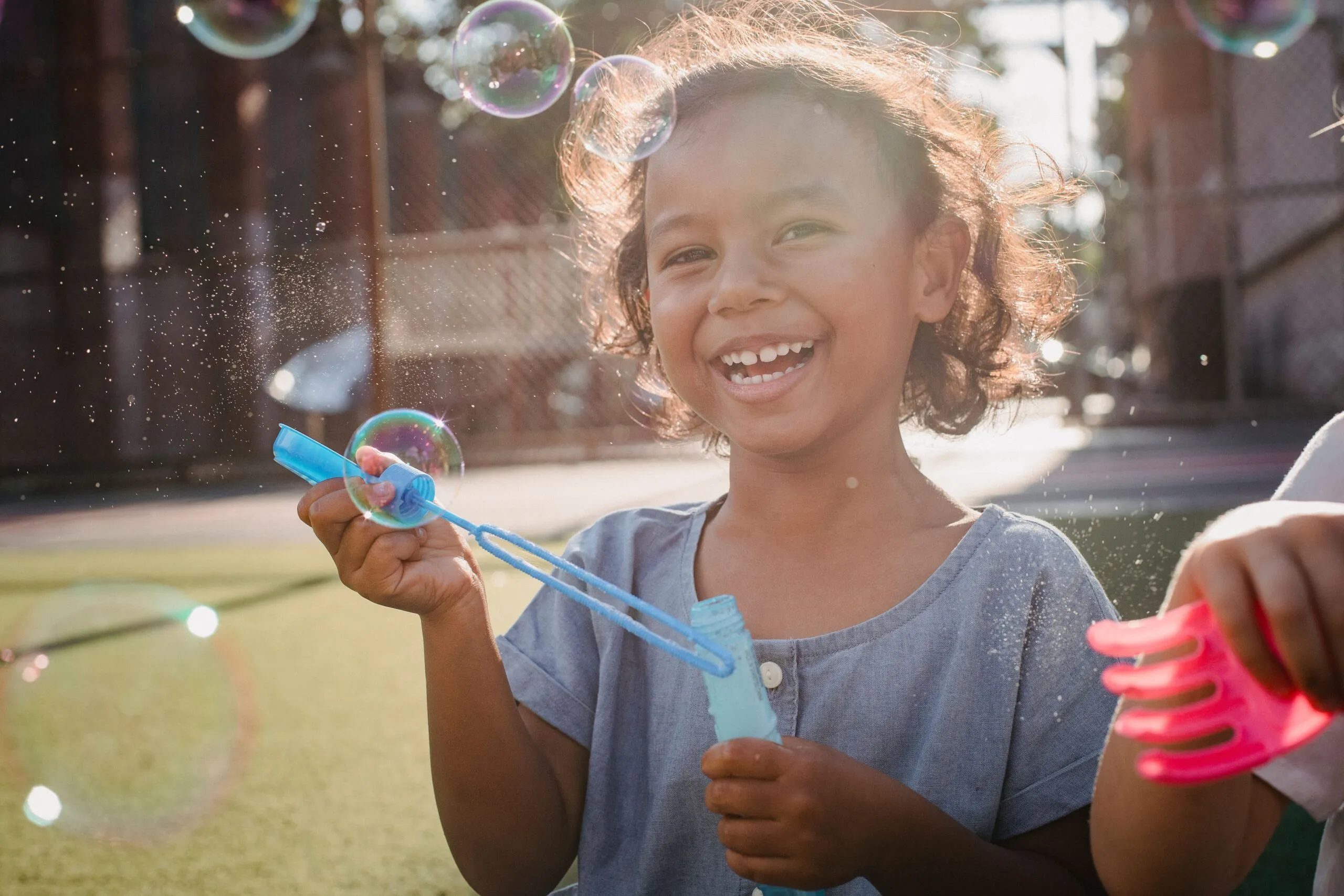 A cheerful young girl enjoys playing with soap bubbles outdoors on a sunny day.