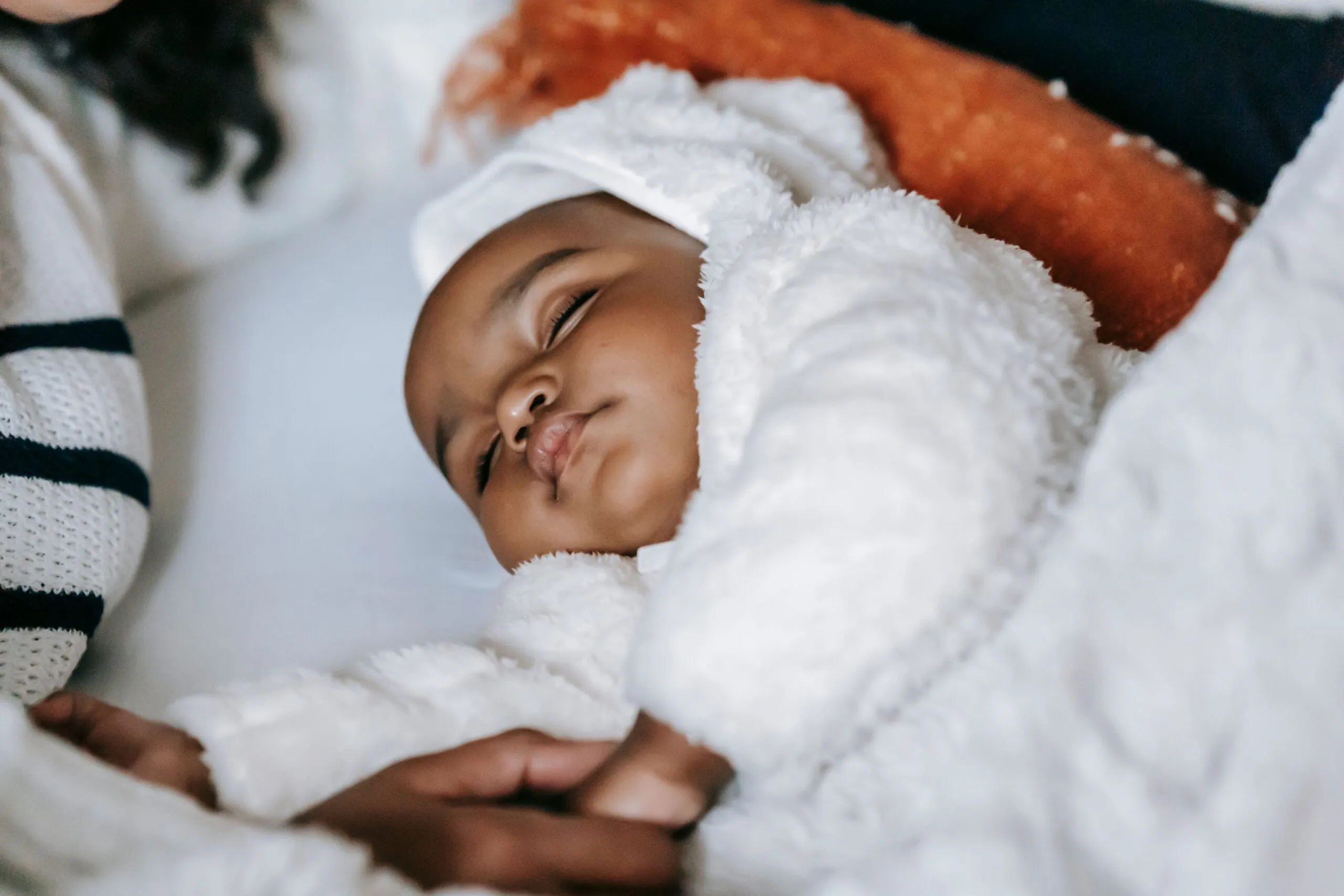From above of crop anonymous African American mother holding hand of cute newborn baby in warm clothes sleeping on cozy bed