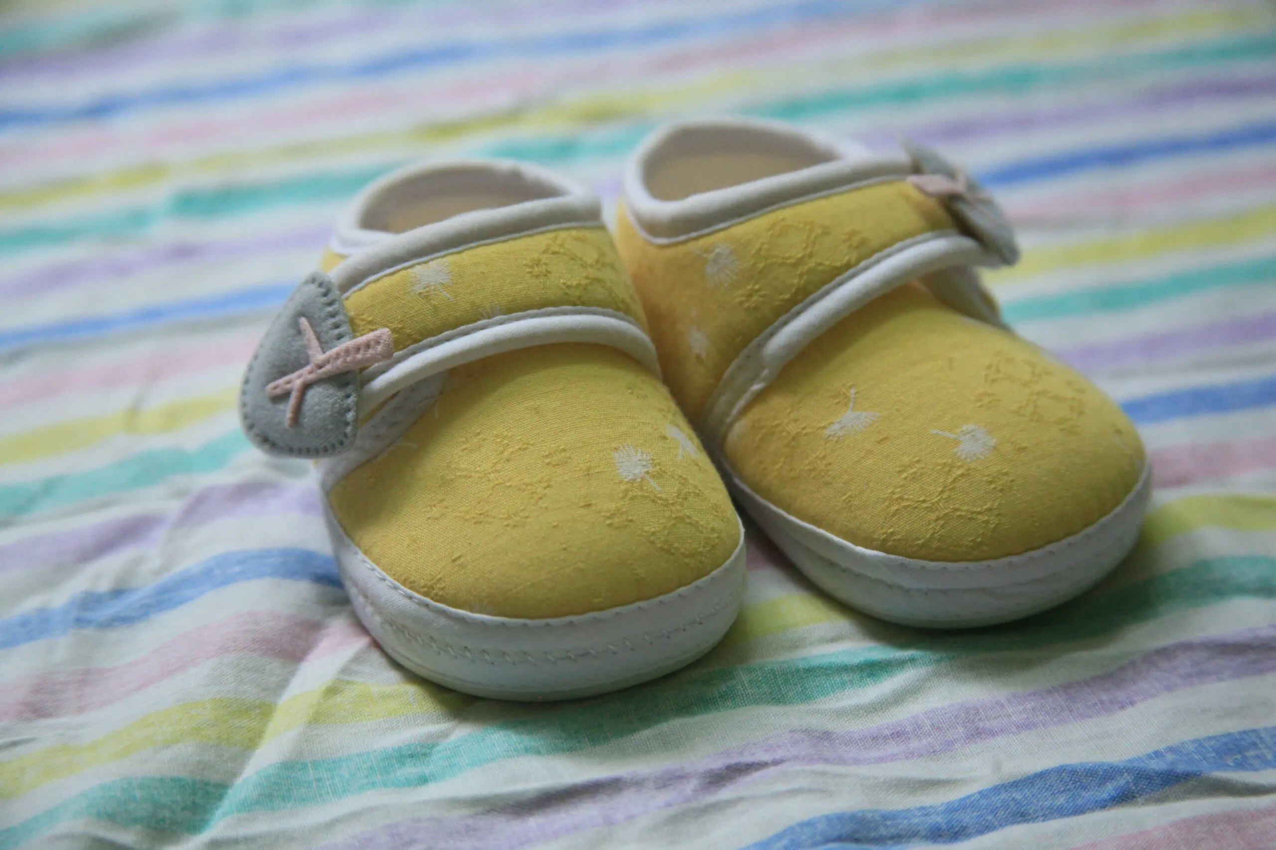 Pair of cute yellow baby shoes with star patterns on a striped blanket.