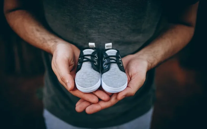 Close-up of male hands holding small baby shoes, representing new fatherhood.