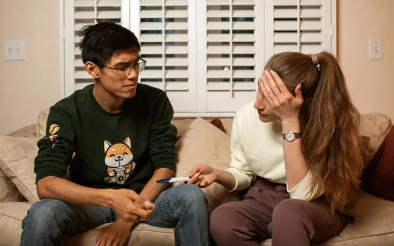 A couple on a couch reacts emotionally to a pregnancy test result, signaling life-changing news.