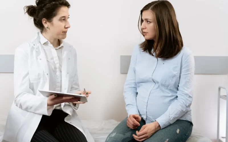 A pregnant woman consulting with a female doctor in a medical clinic setting.