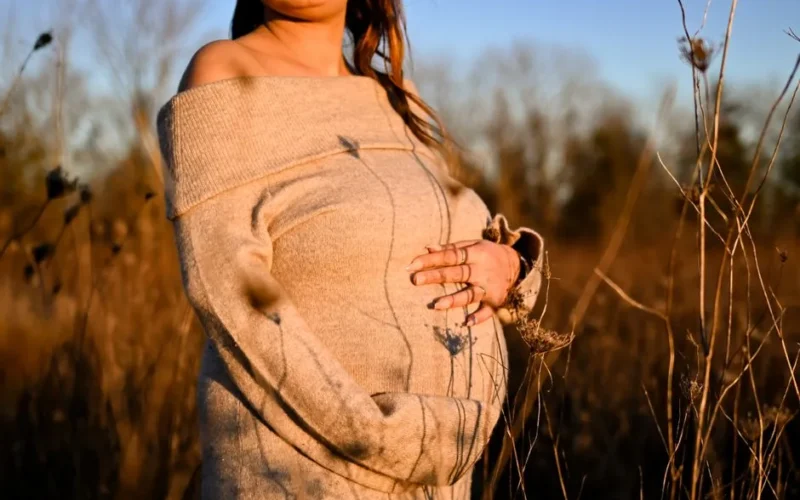 A woman embraces her pregnancy in an autumn field with warm sunlight.