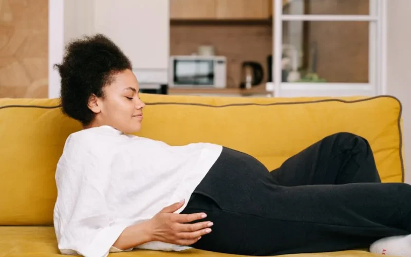 A pregnant woman comfortably rests on a yellow sofa at home, embodying warmth and tranquility.