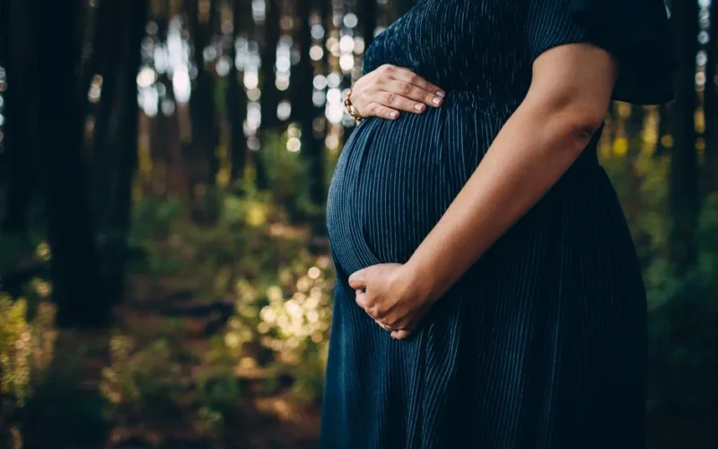 Crop unrecognizable pregnant woman holding tummy with both hands while waiting for childbirth