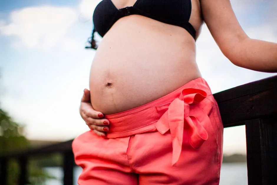 Expectant mother holding her belly, showcasing maternity in a natural outdoor setting.