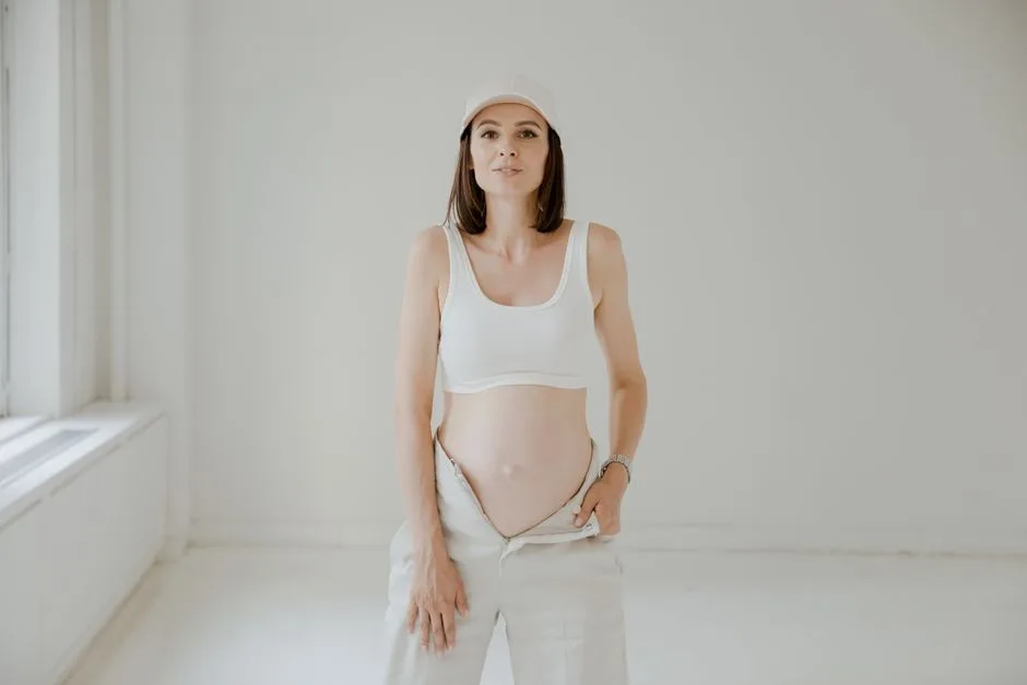 Pregnant woman in white clothing posing indoors with a serene expression.