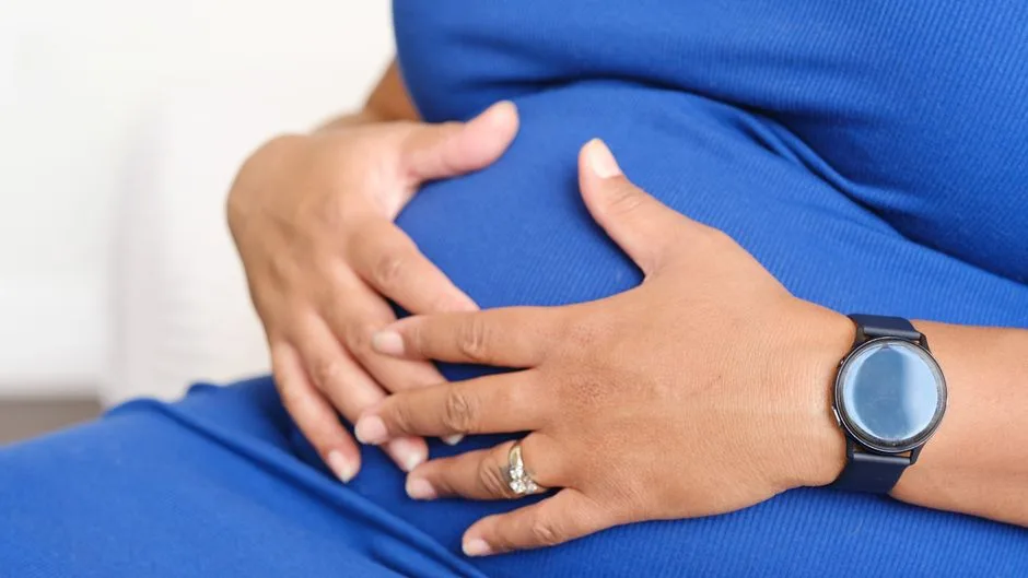 Closeup of a pregnant woman resting her hands on her belly, displaying a watch and a ring.