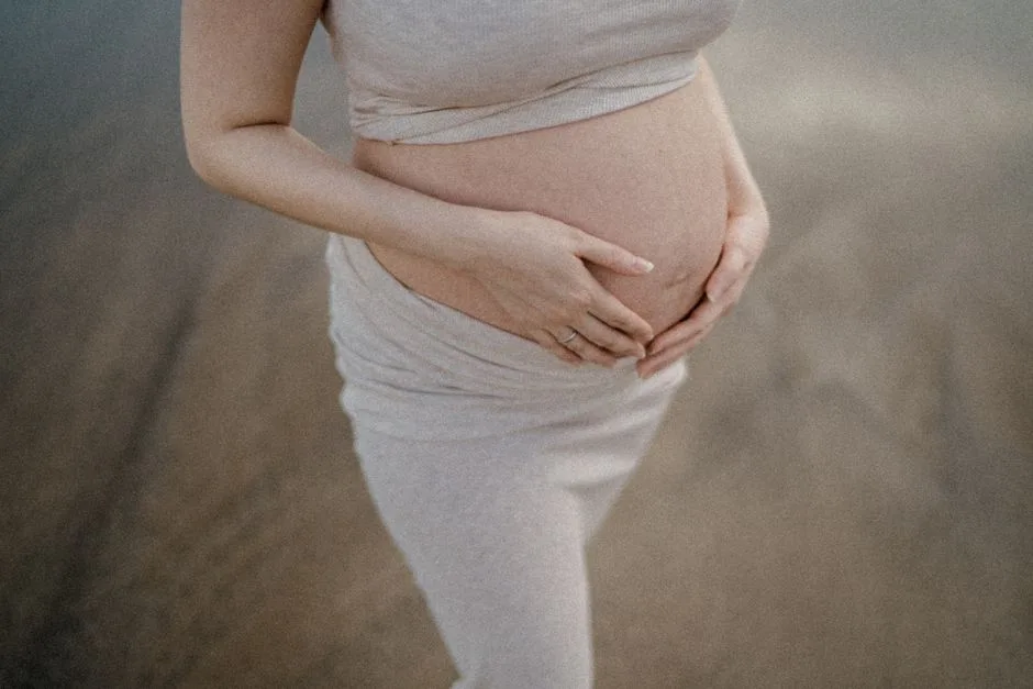 A pregnant woman gently holds her belly while standing outdoors, conveying warmth and serenity.