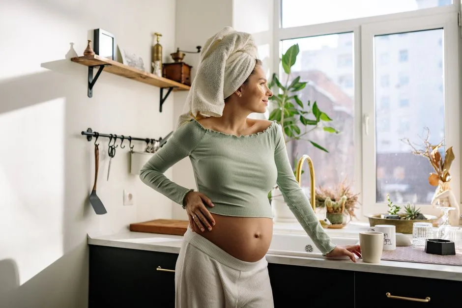 Young pregnant woman enjoys morning in kitchen, gazing outside.