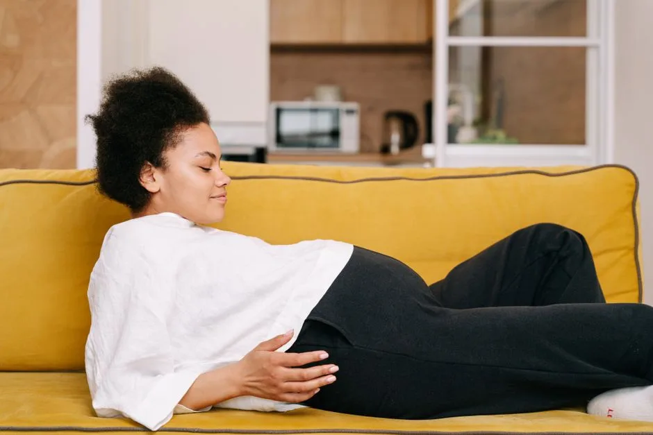 A pregnant woman comfortably rests on a yellow sofa at home, embodying warmth and tranquility.