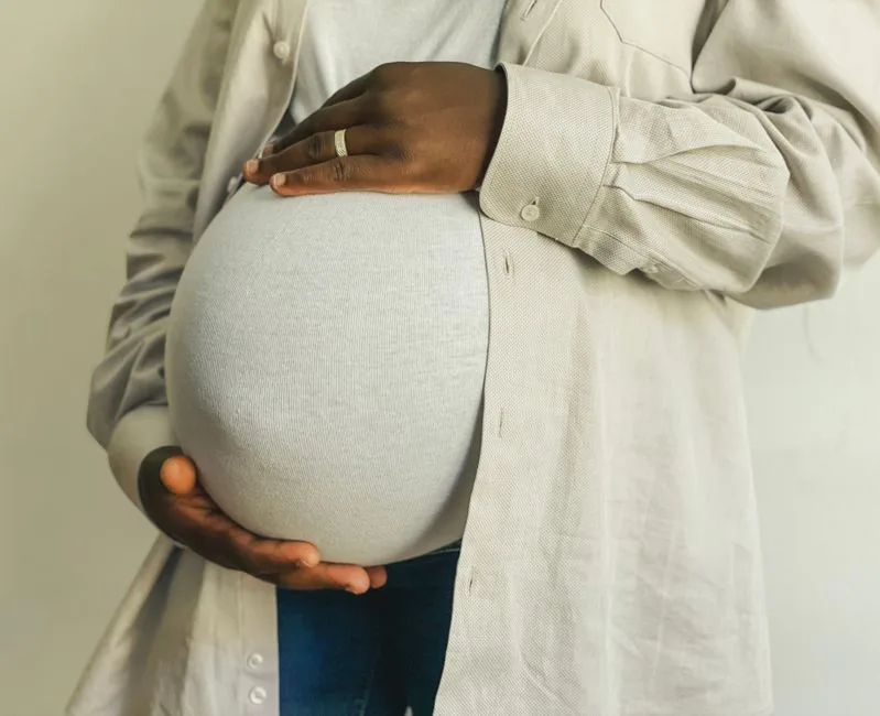 Pregnant woman in casual attire gently holding her belly, symbolizing motherhood.