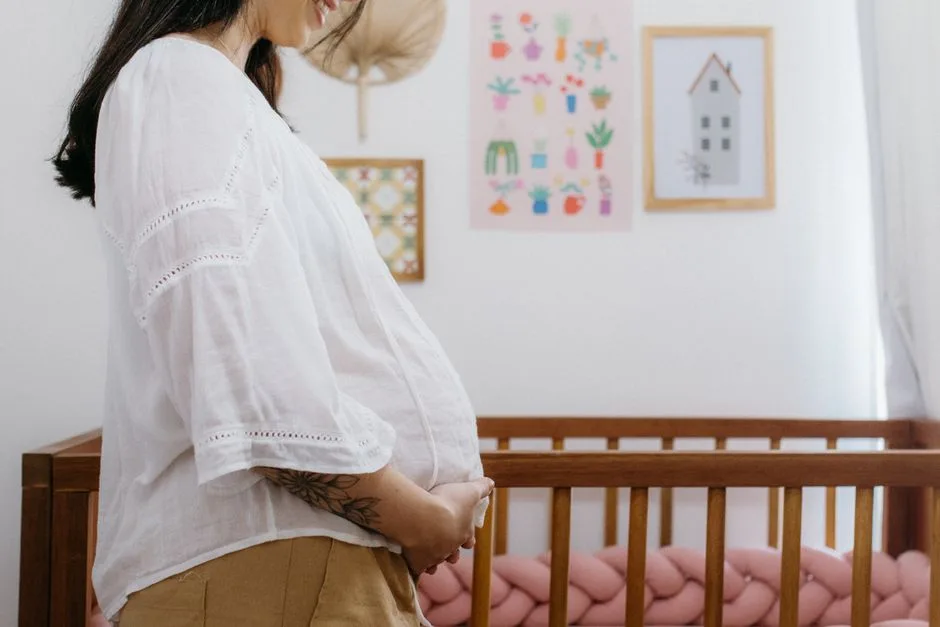 Expectant mother standing beside a wooden crib in a beautifully decorated nursery room.