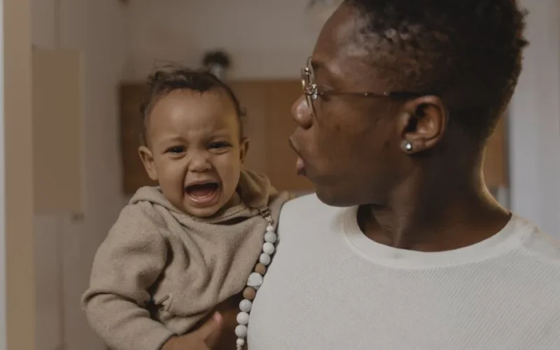 A father soothes his crying baby while holding them indoors.