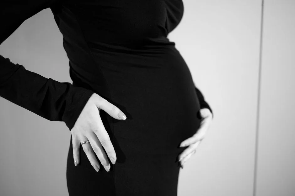 Side view of a pregnant woman gently holding her belly in a black dress.