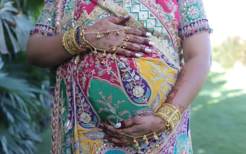 Colorful traditional Indian attire with henna design on a pregnant woman's belly outdoors.