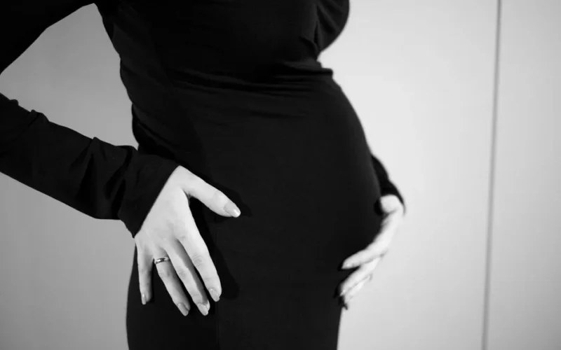 Side view of a pregnant woman gently holding her belly in a black dress.