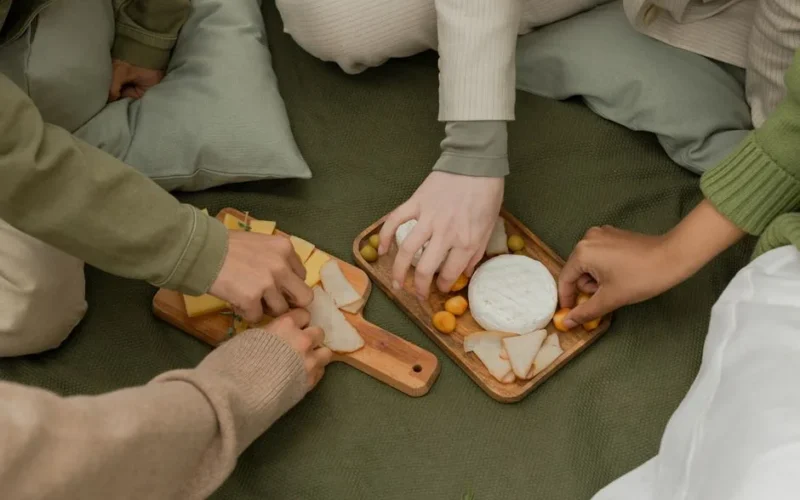 A group of friends sharing and enjoying a delicious cheese platter during an outdoor picnic.