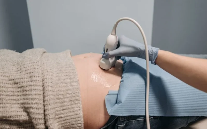 A healthcare professional performing an ultrasound on a pregnant abdomen.