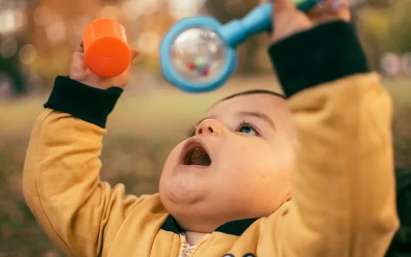 Cute baby playing outdoors with a colorful toy, enjoying the autumn day.