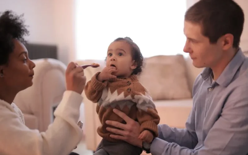 A caring family moment where parents feed their baby in a cozy living room setting.
