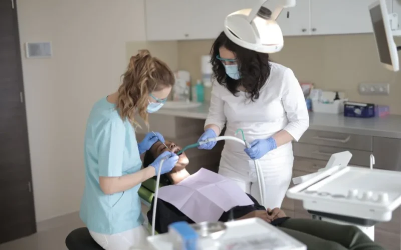Female dentists in medical masks and latex gloves wearing uniform using medical instruments while treating teeth of female patient in modern dental clinic