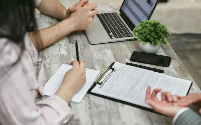 Professionals discussing home insurance policy over laptop and notes in an office setting.