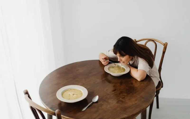 A woman sits alone savoring hot soup at a rustic table, creating a serene dining atmosphere.