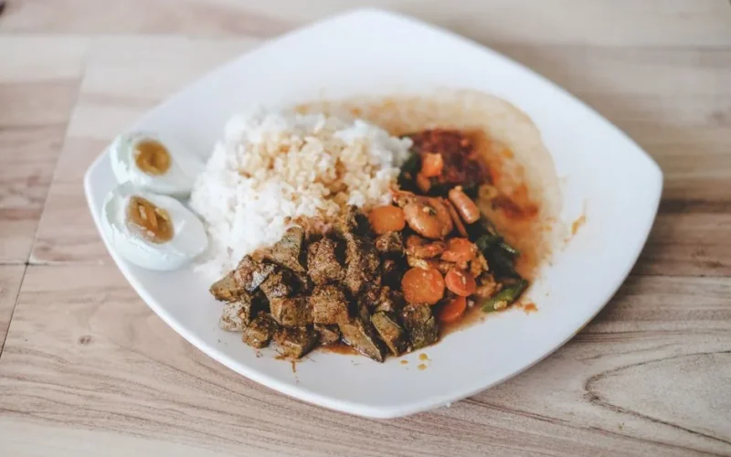 A tasty Asian dish featuring rice, spicy vegetables, liver, and salted egg on a white plate.