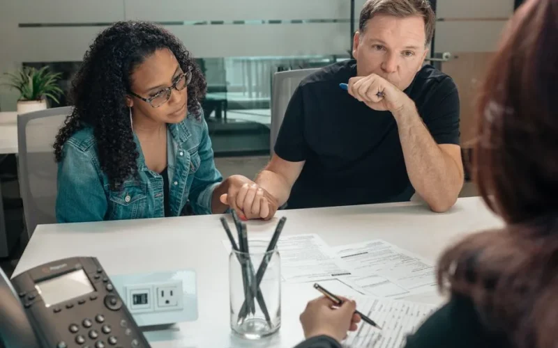 A couple discusses adoption process with an advisor in a modern office setting.