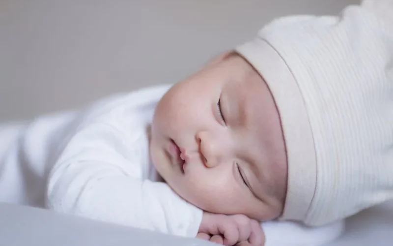 Close-up of a peaceful baby sleeping in a cozy white outfit and hat, showcasing innocence and serenity.