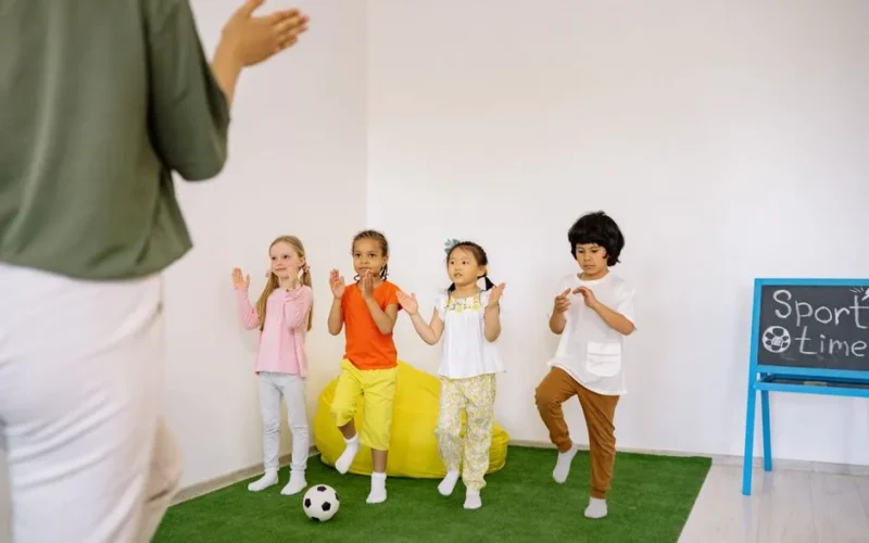 A group of preschool children participating in a fun indoor sports activity led by a teacher.