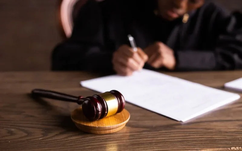 Judge signing documents at desk with focus on gavel, representing law and justice.