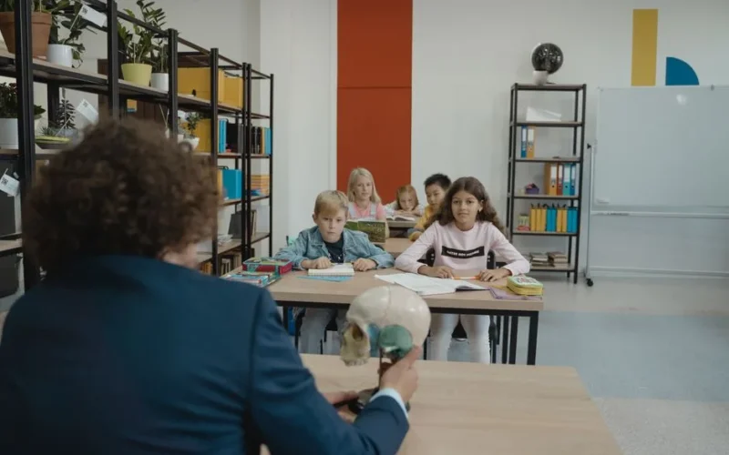 Children learn biology in a colorful classroom setting with a teacher explaining a skull model.