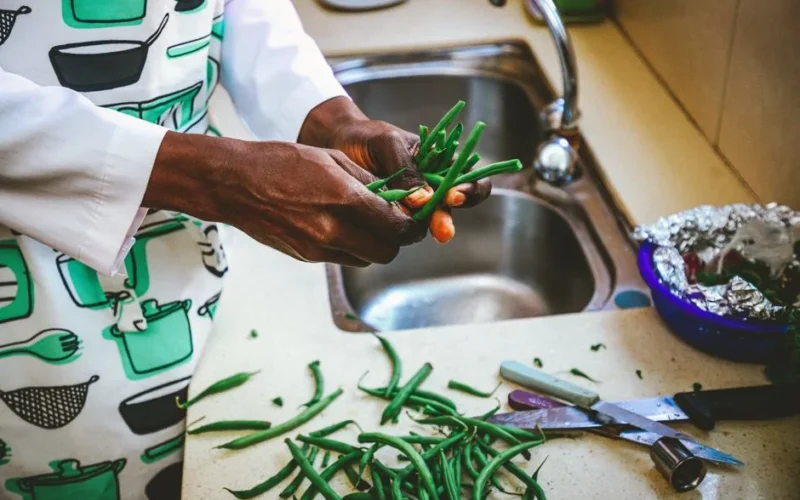 Hands of a chef preparing fresh green beans on a kitchen countertop near a sink.
