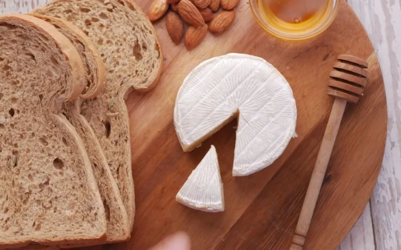 Rustic breakfast platter with brie cheese, almonds, and honey on a wooden board.
