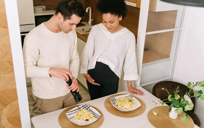 A pregnant couple preparing pasta in a cozy kitchen setting.