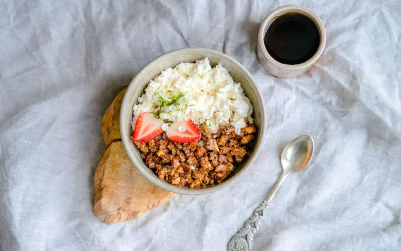 A delicious breakfast bowl with cottage cheese, granola, and strawberries served with black coffee.