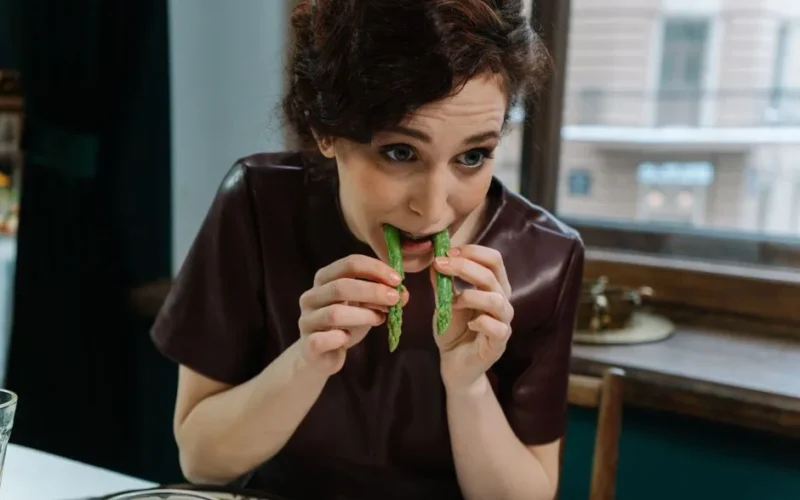 Woman dining on fresh asparagus indoors, embracing healthy eating habits.
