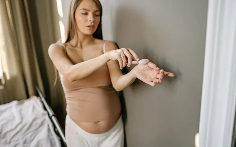 Pregnant woman in bedroom using a jade roller for self-care. Emphasizes wellness and relaxation.