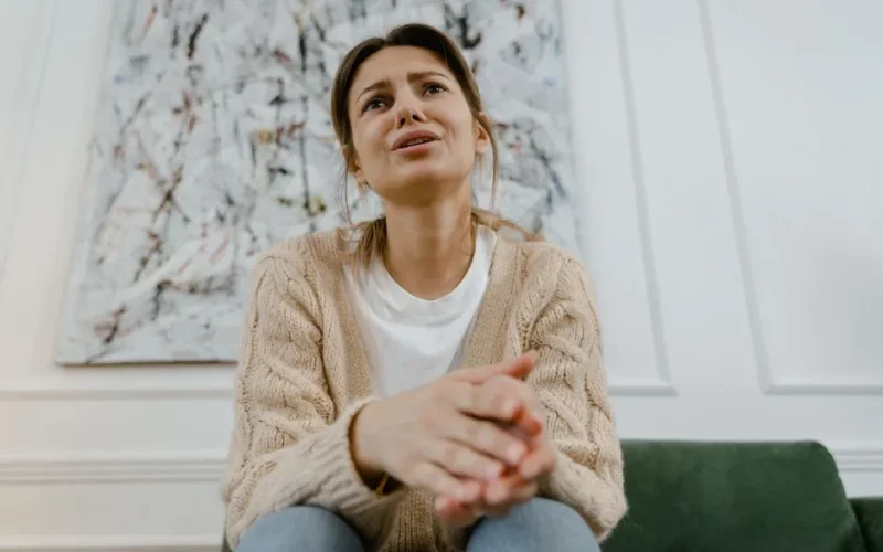 A woman in a cozy sweater is sitting indoors, expressing distress and frustration.