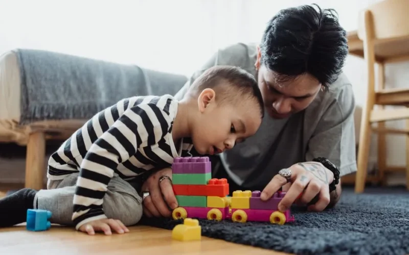 A father and son bonding while playing with colorful blocks indoors.