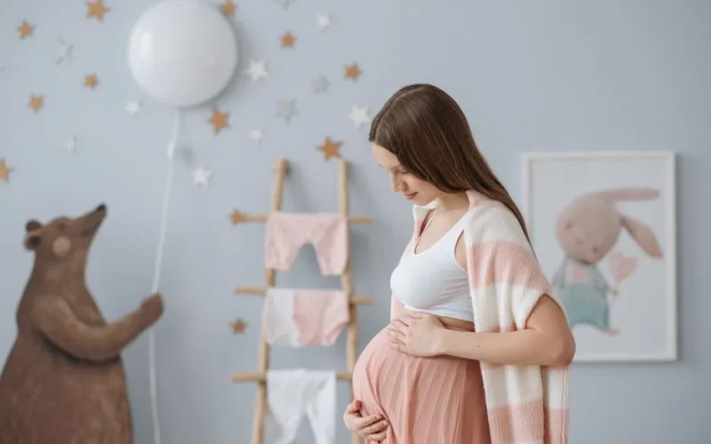 Side view of expectant mother in a cozy nursery with soft pastel decor.