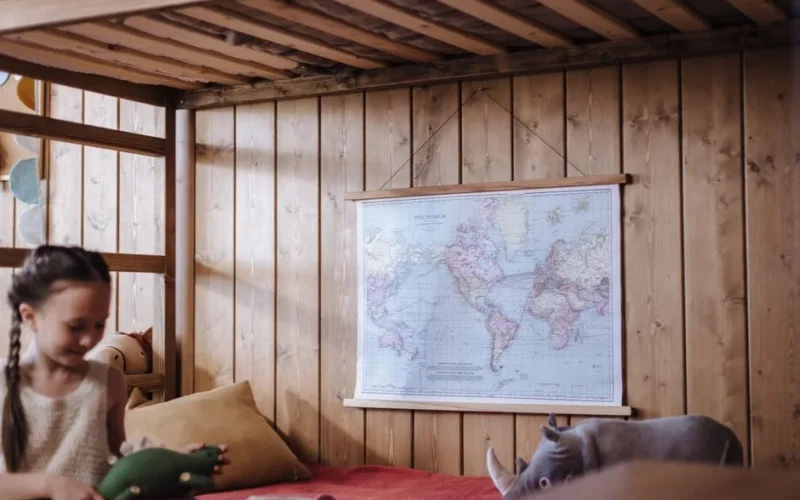 A cheerful child in a wooden bedroom with a map, playing with toys.